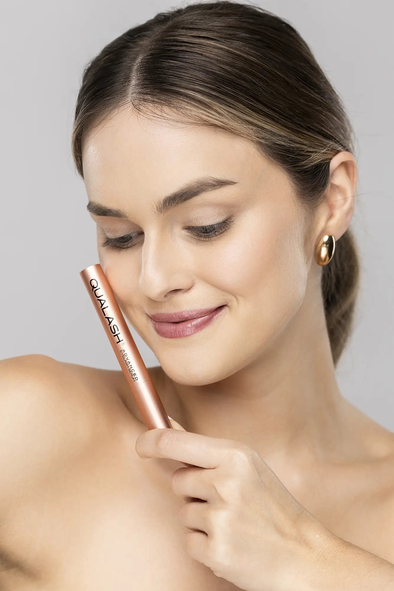 Smiling woman holding QUALASH Advanced Eyelash Serum